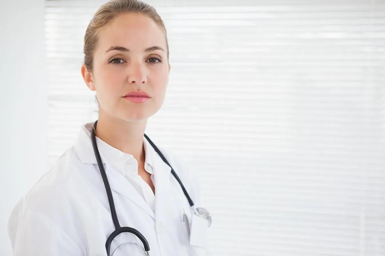 Female doctor in her 50s standing in modern kitchen, looking concerned while holding up old non-stick pan next to new titanium pan